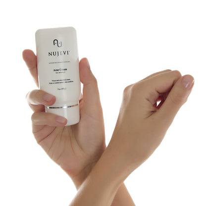 Crossed woman's hands holding a tube of acne cream.
