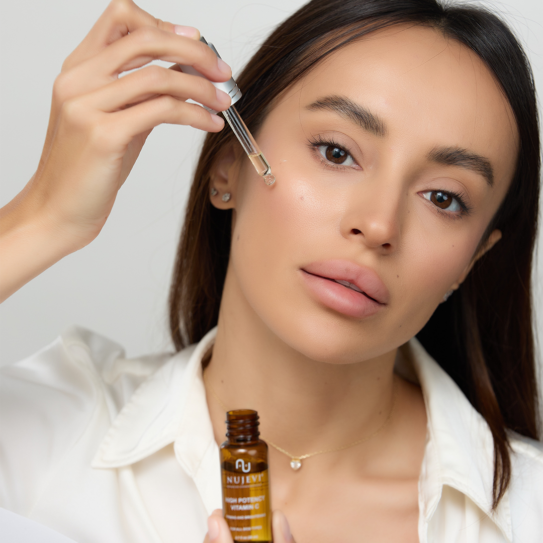 Woman's hand holding Vitamin-C dropper dispensing the liquid on her face.