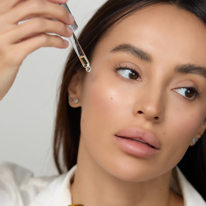 Woman's hand holding Retinol-C dropper dispensing the liquid on her face.